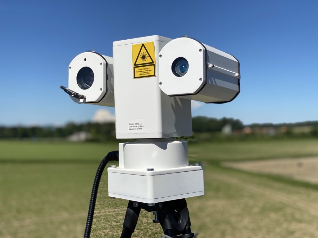Y1188A tracking camera: a white pan-tilt unit with two lenses and a laser warning label